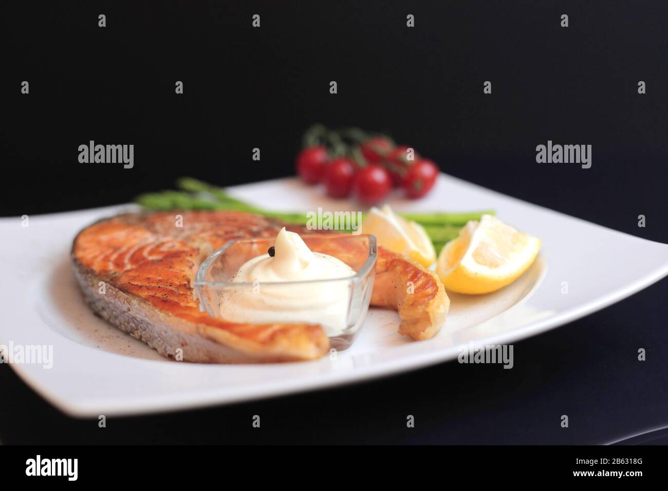 Lachssteaks mit Gemüse und Gewürzen: Spargel, Tomaten, Ingwer, Pfefferkörner, Salz, Chili, Zwiebel, Zitrone und Olivenöl auf schwarzem Grund. Heilen Stockfoto