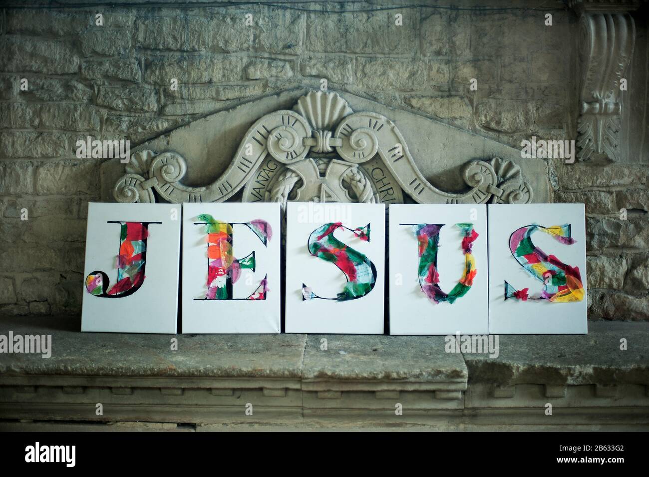 Auf einem Stein in einer Kirche mit fünf Kartonkarten mit einem koluierten Buchstaben auf jeder Rechtschreibung des Wortes Jesus. Stockfoto
