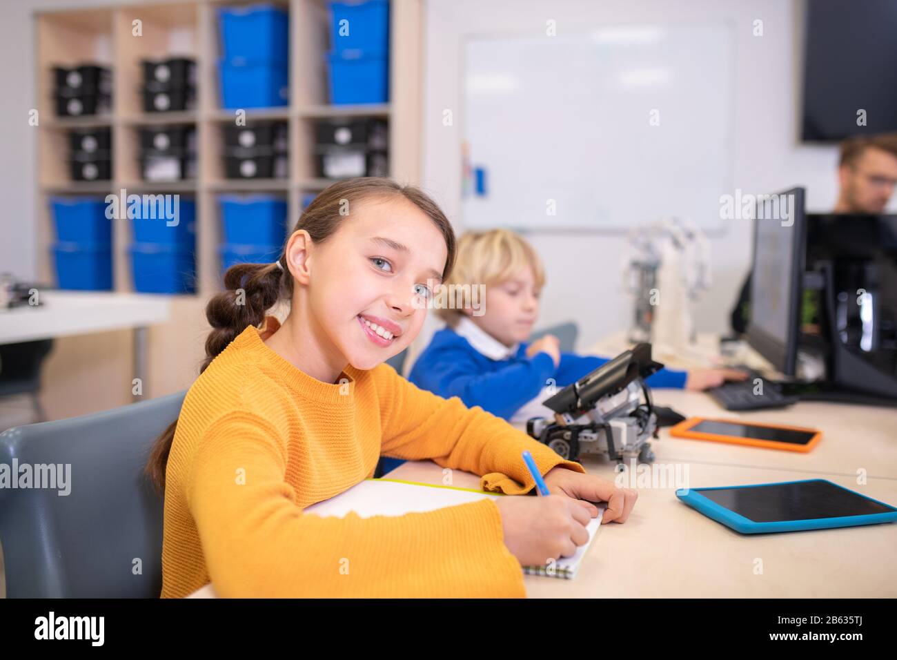 Schüler sitzen am Schreibtisch, Mädchen nimmt Notizen, Junge tippen Stockfoto