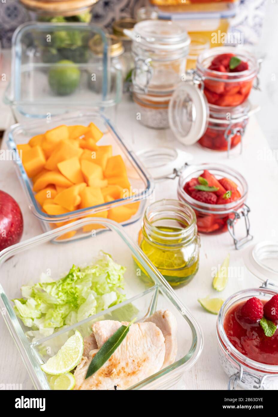 Batch-Kochszene voller Behälterbrille mit köstlicher Mahlzeit im Inneren auf einem weißen Holztisch. Stockfoto