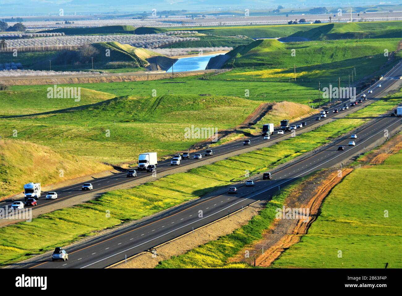 Interstate Highway I5 im zentralen Tal des CA-Verkehrs, California Aqueduct Water im Hintergrund und weiße Bäume von Almond Bloom in Richtung Norden links Stockfoto