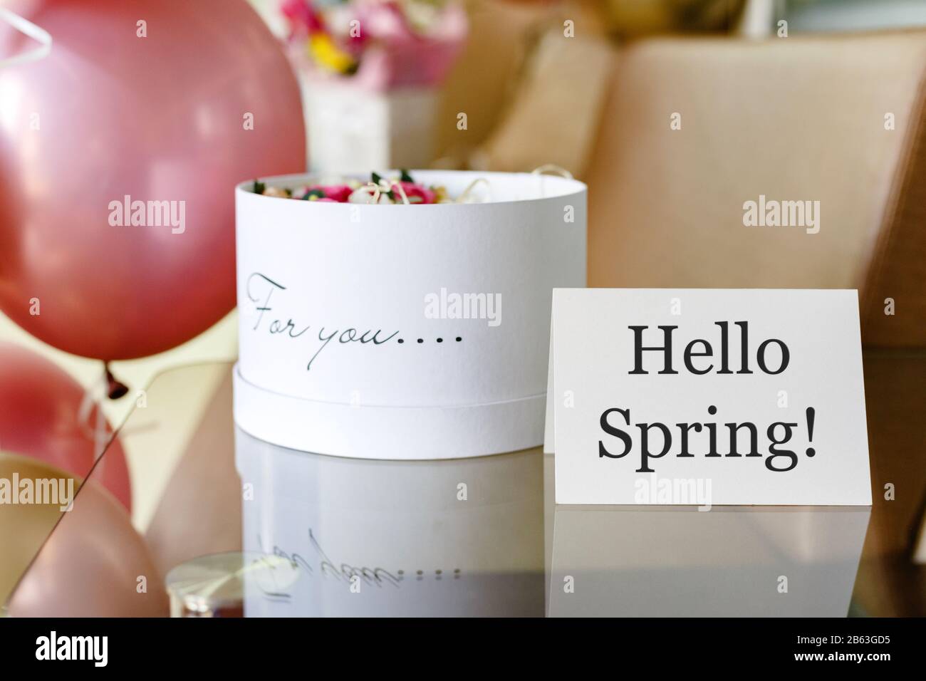Text Hello Spring auf weißer Karte mit Blumenkasten. Weißer Hut runder Kasten mit rosa Rosen Blumen und Text Für Sie. Festliche Ballons in Pink und Gold. Stockfoto