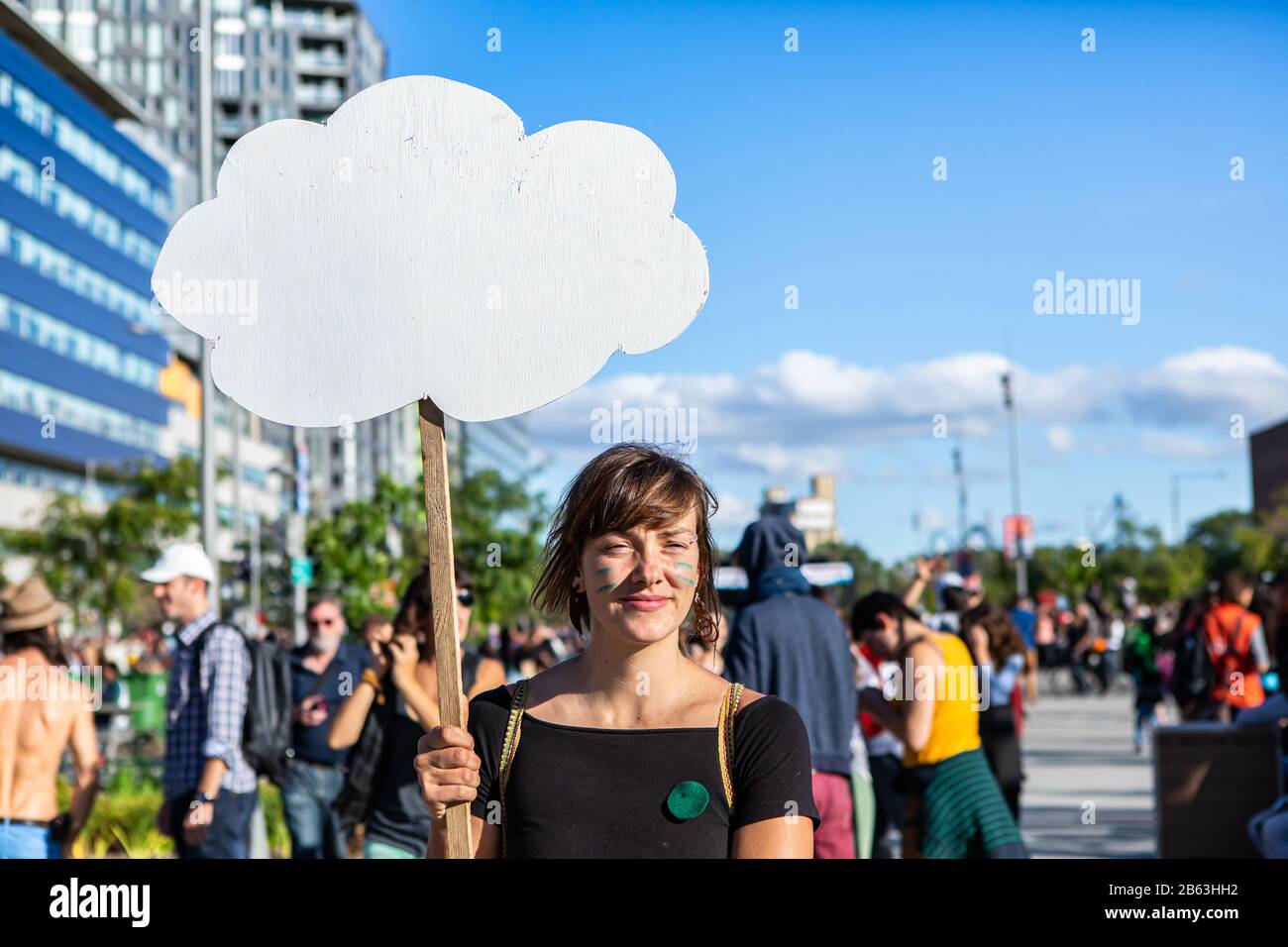 Ein Nahschuss von einer jungen Frau, die bei einer Kundgebung zum Klimawandel ein wolkenförmiges leeres Protestschild hält, Platz für Kopien gegen einen blauen Himmel Stockfoto