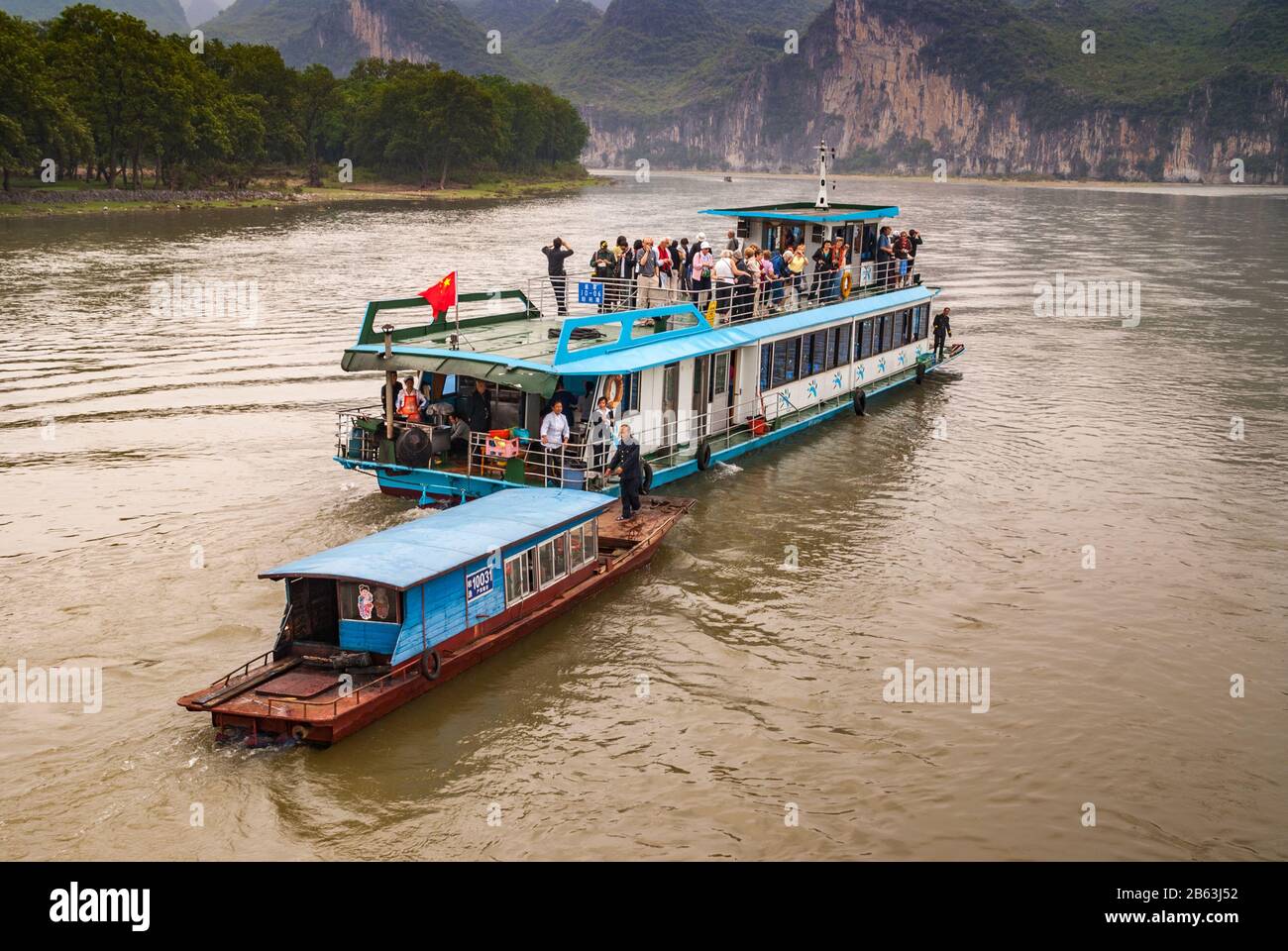 Guilin, China - 10. Mai 2010: Entlang Des Flusses Li. Anbieter auf kleinem Boot nähert sich auf braunem blau-weißem Touristenschiff an. Felsklippen und g Stockfoto