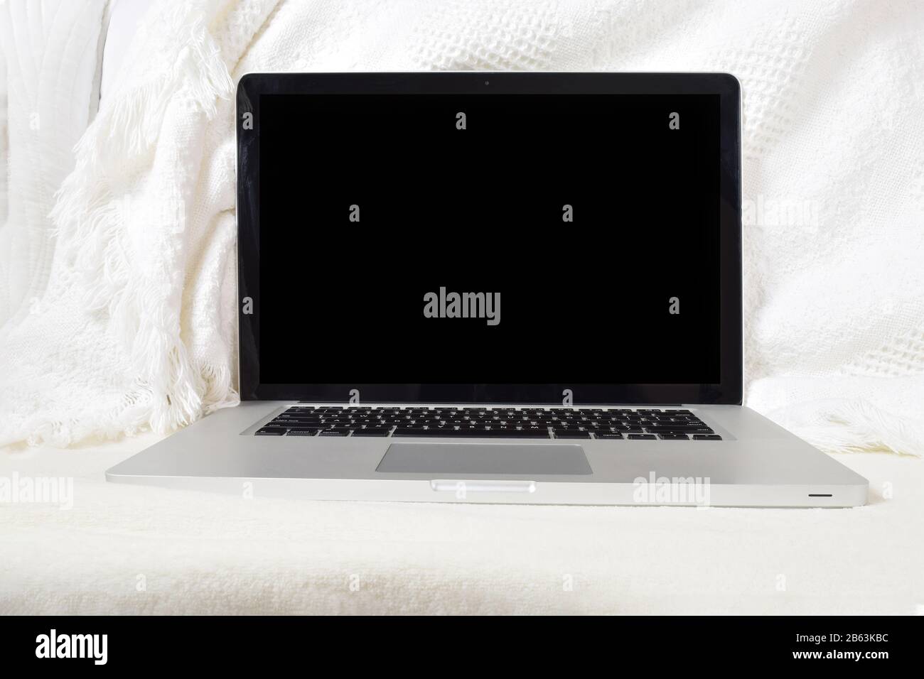 Moderner Laptop, der sich auf einer weichen weißen Decke auf der Couch entspannen kann. Verfügt über einen Beschneidungspfad im Bildschirm, um das Hinzufügen eines eigenen Bildes zum Bildschirm zu erleichtern. Stockfoto