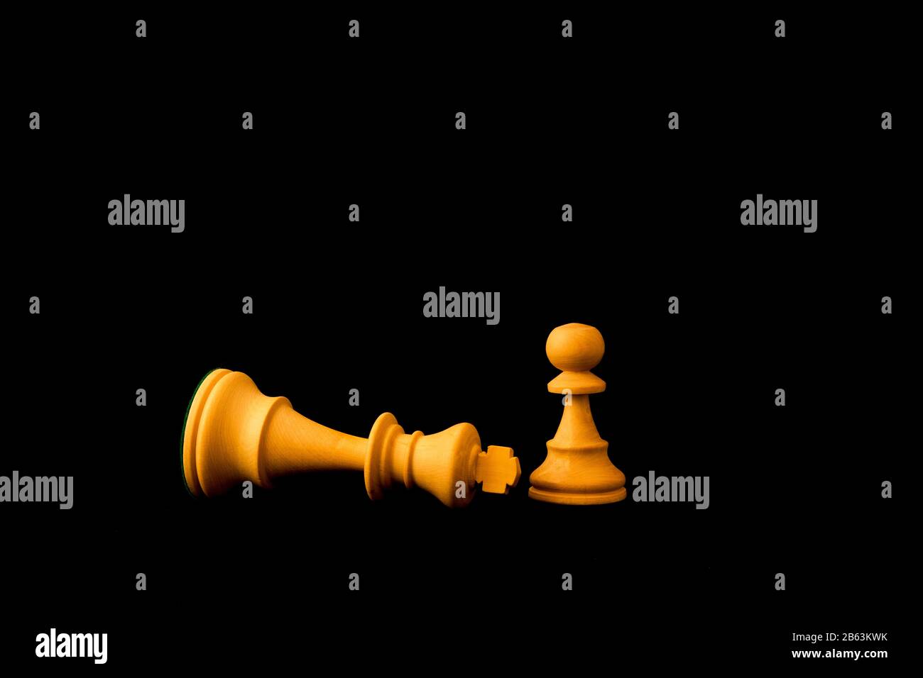 König gibt sich dem Pfandleiher, da die kleinen und Schwachen das große und mächtige Konzept besiegen können. Zwei standardmäßige Schach-Holzstücke auf schwarzem Hintergrund Stockfoto