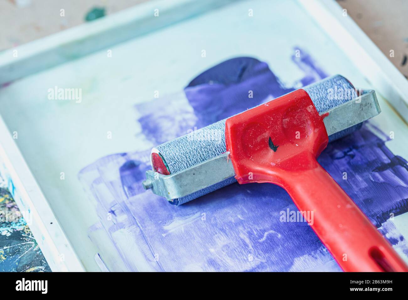 Rote Tintenwalze und gespritzter blauer Lack im Fach - kreative Druckwerkzeuge Stockfoto