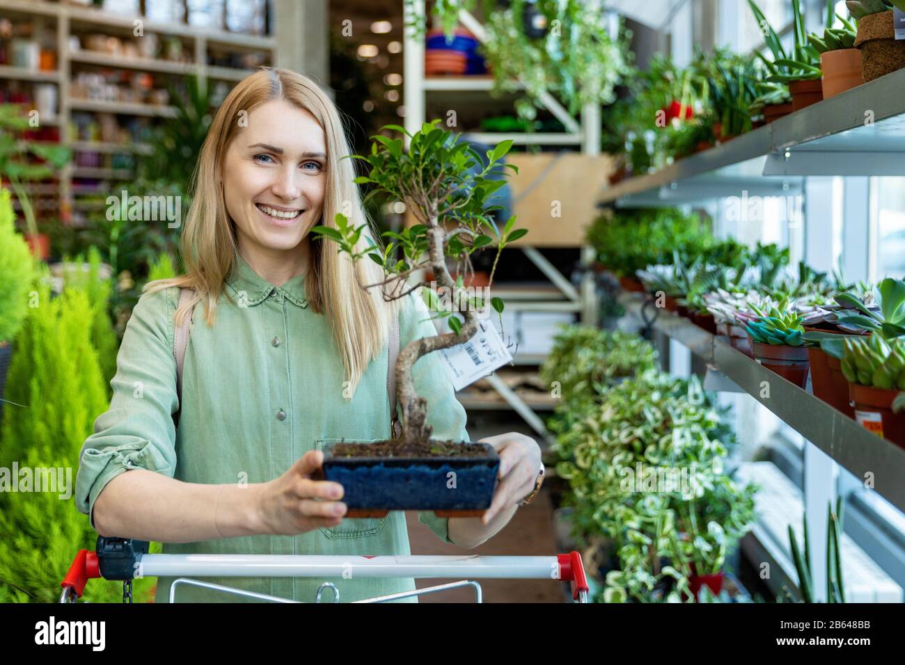 Lächelnde Frau mit Bonsai-Baum im Gartencenter Stockfoto