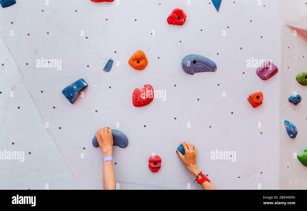 Kletterin junge Frau beginnt mit einer Boulderbahn an einer künstlichen Wand in der Halle, Hände liegen in der Nähe Stockfoto