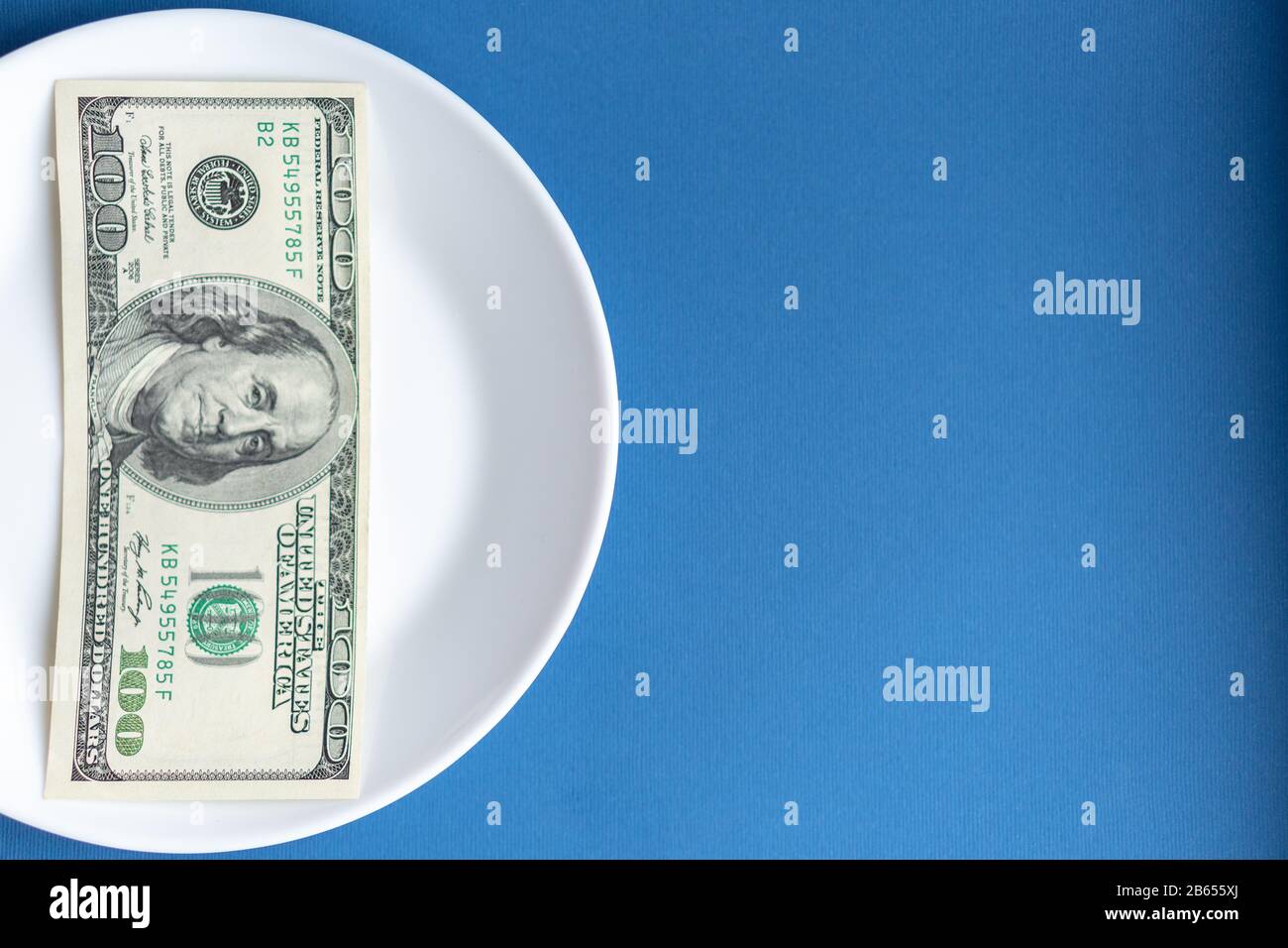 Medikamente Kosten Geld. Drogen und Dollar. Weiße Platte mit mehrfarbigen Pillen und Kapseln und einer 100-Dollar-Rechnung auf einem klassischen blauen Hintergrund. Pillen Stockfoto
