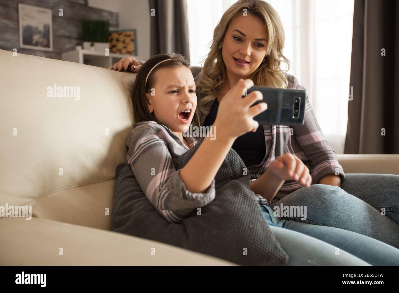 Süßes kleines Mädchen schockiert, nachdem sie ein beunruhigendes Online-Video auf dem Handy neben ihrer Mutter gesehen hat. Moderne Mutter. Stockfoto