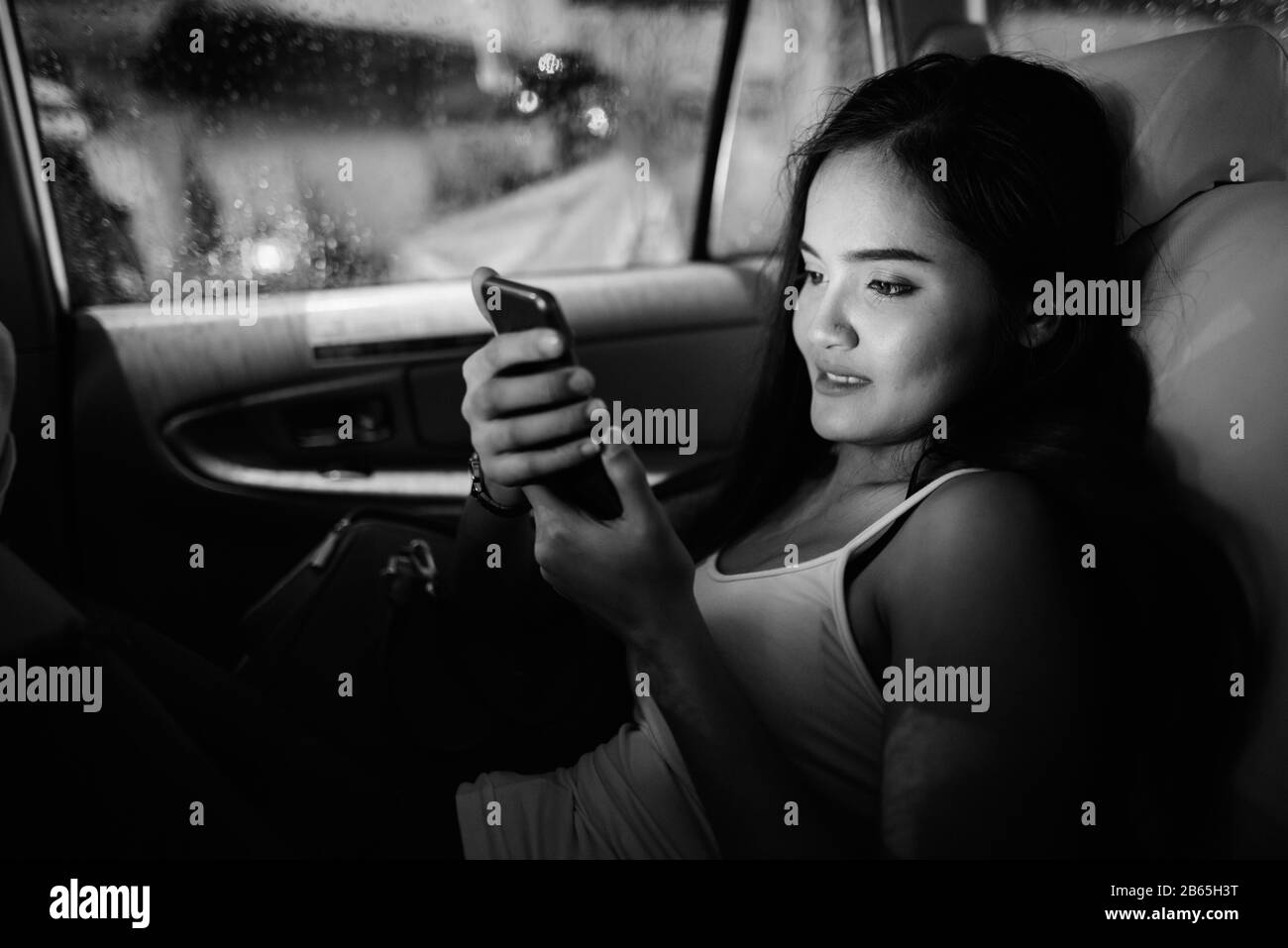 Fröhliche junge, schöne asiatische Touristenfrau, die im Auto telefoniert Stockfoto