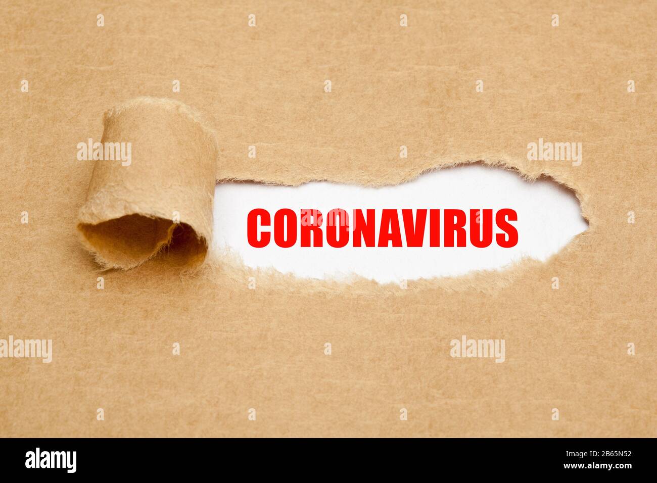 Gedrucktes Wort Coronavirus, das hinter zerrissenem braunem Papier erscheint. Covid-19-Konzept für den Ausbruch einer Virus-Epidemie. Stockfoto