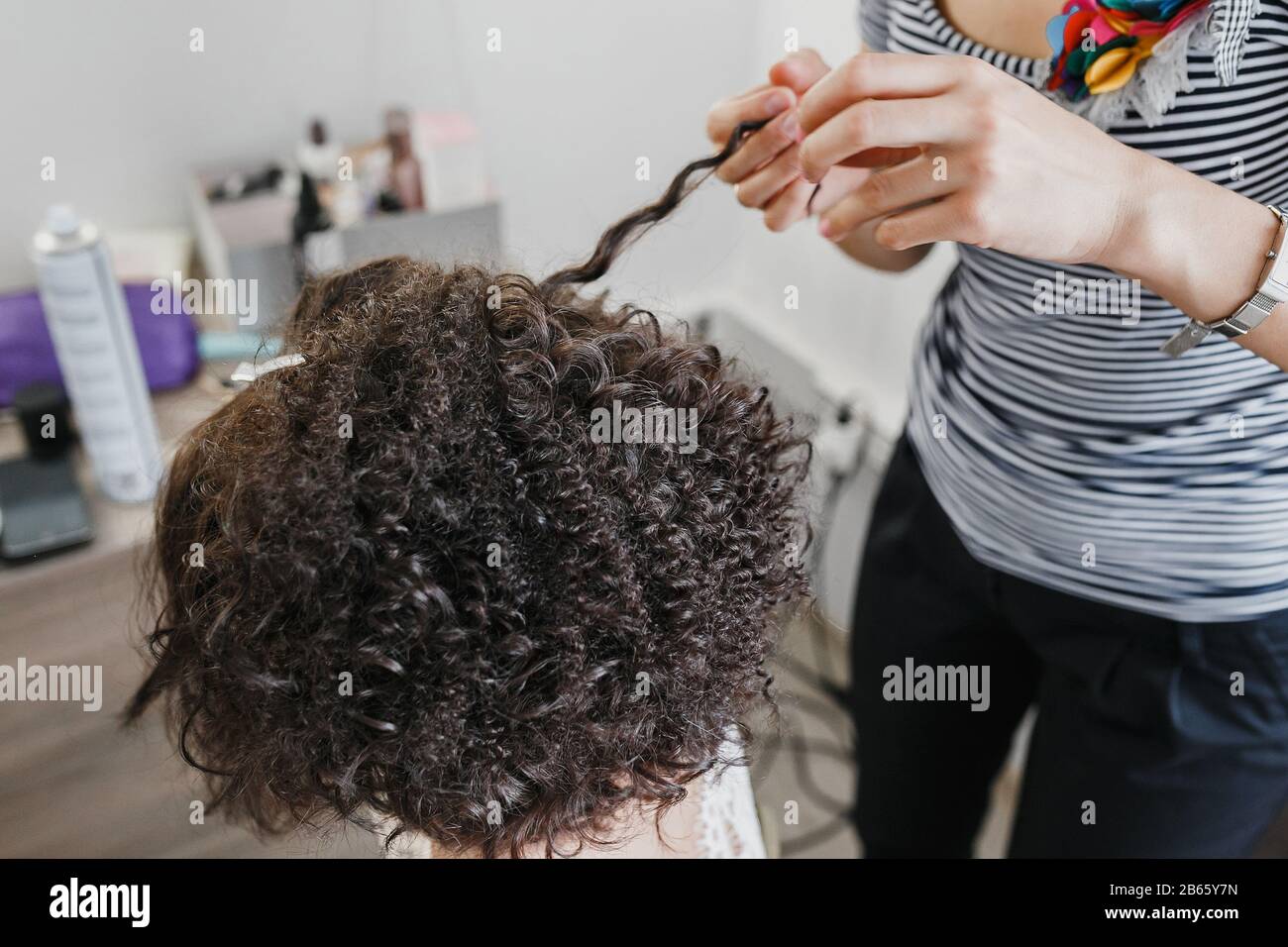 Nahaufnahme eines Friseursalons, der kurze schwarze Haare mit Haarbügeln kräuselt. Stockfoto