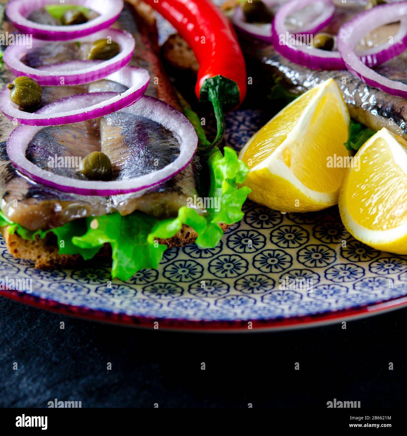 Ein norwegischer junger Heringsschmorrebrod mit Salat, blauer Zwiebel, Zitrone und Sesam liegt auf einer Holzplatte. Nahaufnahme Stockfoto