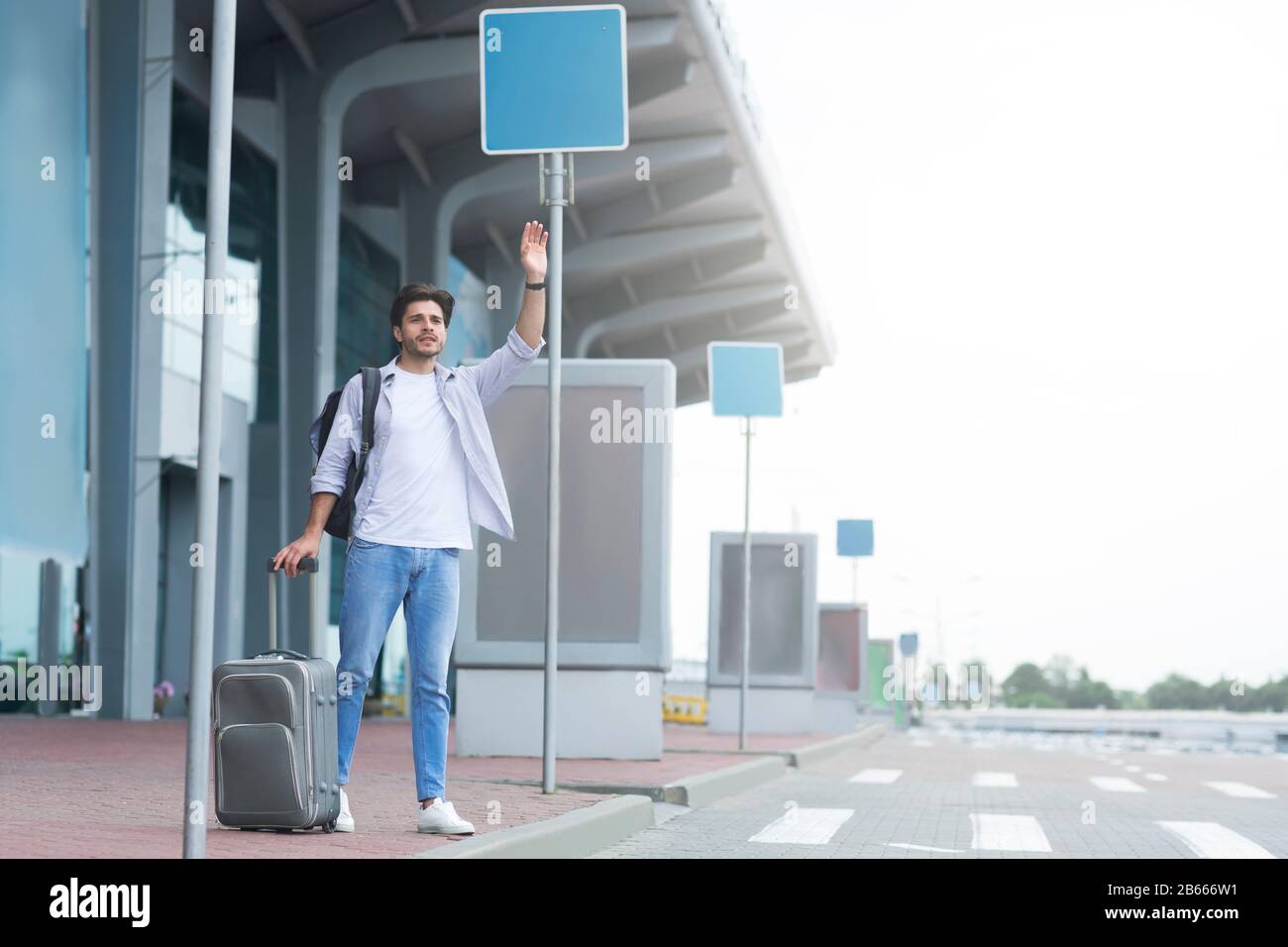 Kabine verfangen. Männlicher Reisender, der in der Nähe des Flughafens steht, winkt Hand und ruft Taxi Stockfoto