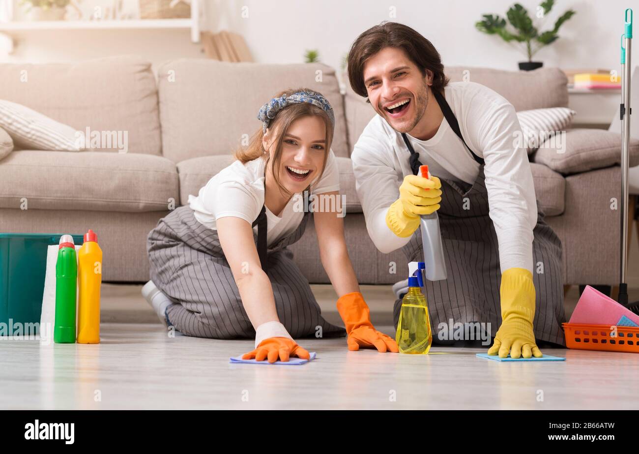 Junges glückliches Paar in Gummihandschuhen Reinigungsboden in ihrer Wohnung Stockfoto