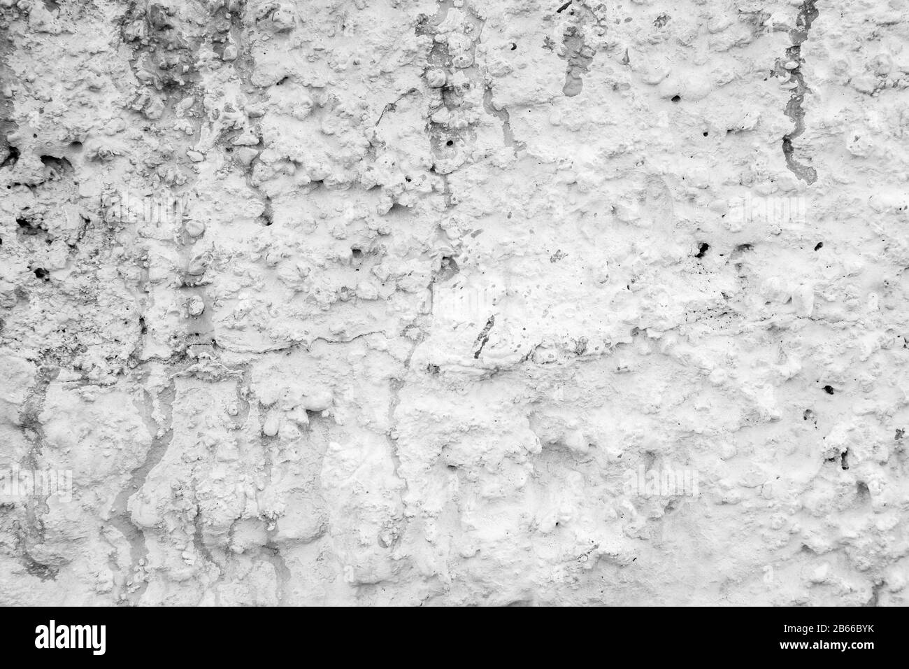 Nahaufnahme einer in Weiß gemalten, rauen und verputzten Stuckwand. Tropfen und Flecken von Farbe. Hochauflösender strukturierter Hintergrund in Schwarzweiß. Stockfoto
