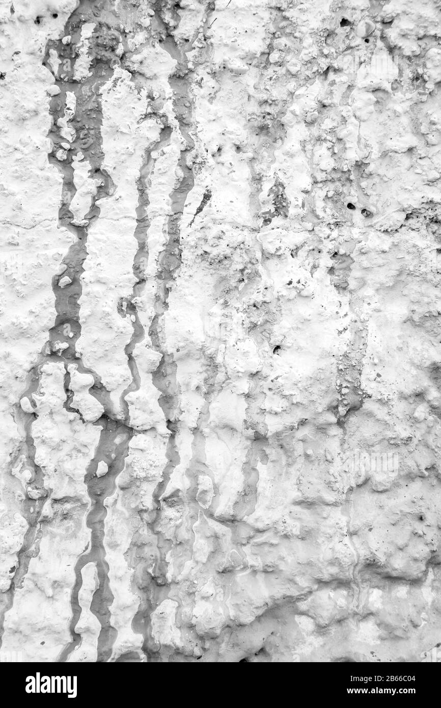 Nahaufnahme einer in Weiß gemalten, rauen und verputzten Stuckwand. Lack tropft und Flecken. Hochauflösender, strukturierter Vollformatshintergrund in Schwarzweiß. Stockfoto