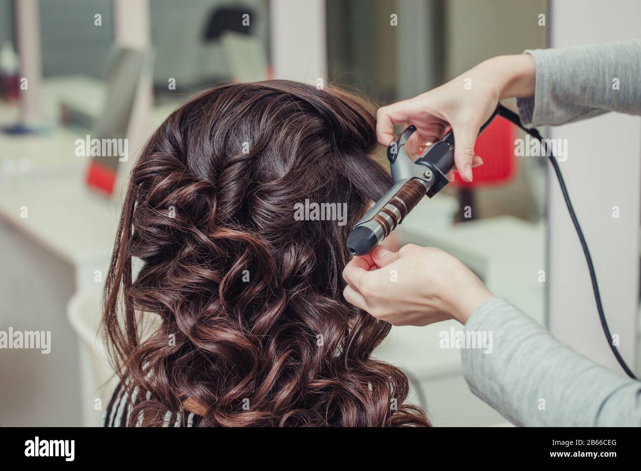 Friseursalon, der sich in einem Kosmetiksalon mit Bügeleisen um das kräuselnde Brunetthaar wickelt Stockfoto