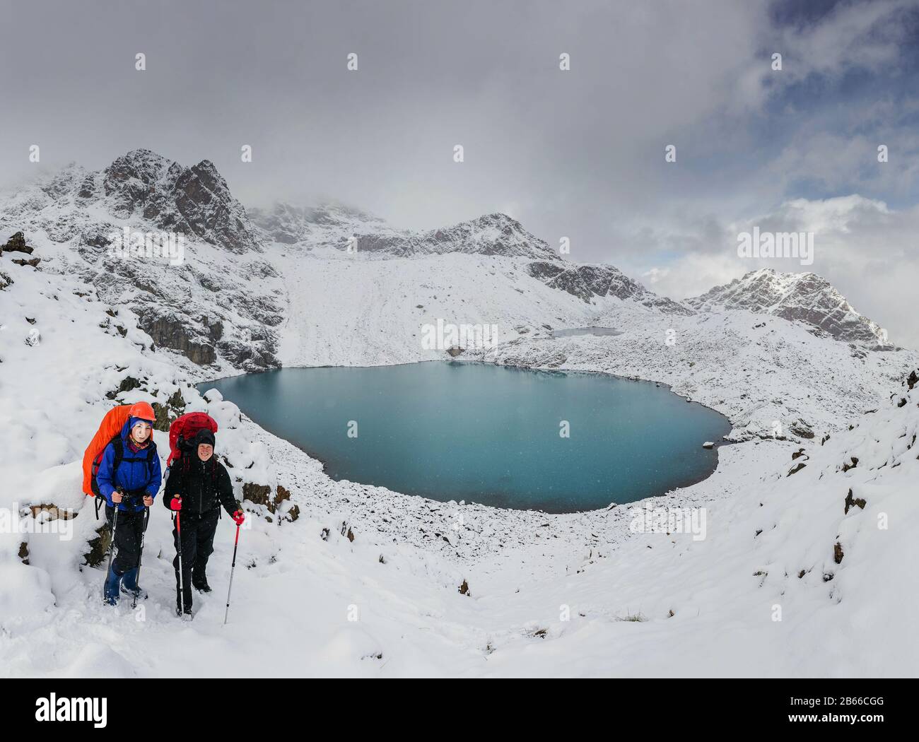 Zwei Wanderer fühlen sich klein vor dem riesigen blauen Bergsee in winterlichen verschneiten Bergen stehend Stockfoto