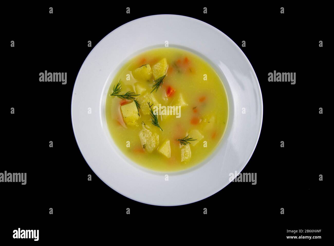 Weiße Milchsuppe mit Kartoffeln, Karotten, Grüns steht in einer weißen Platte, die auf schwarzem Grund isoliert ist Stockfoto