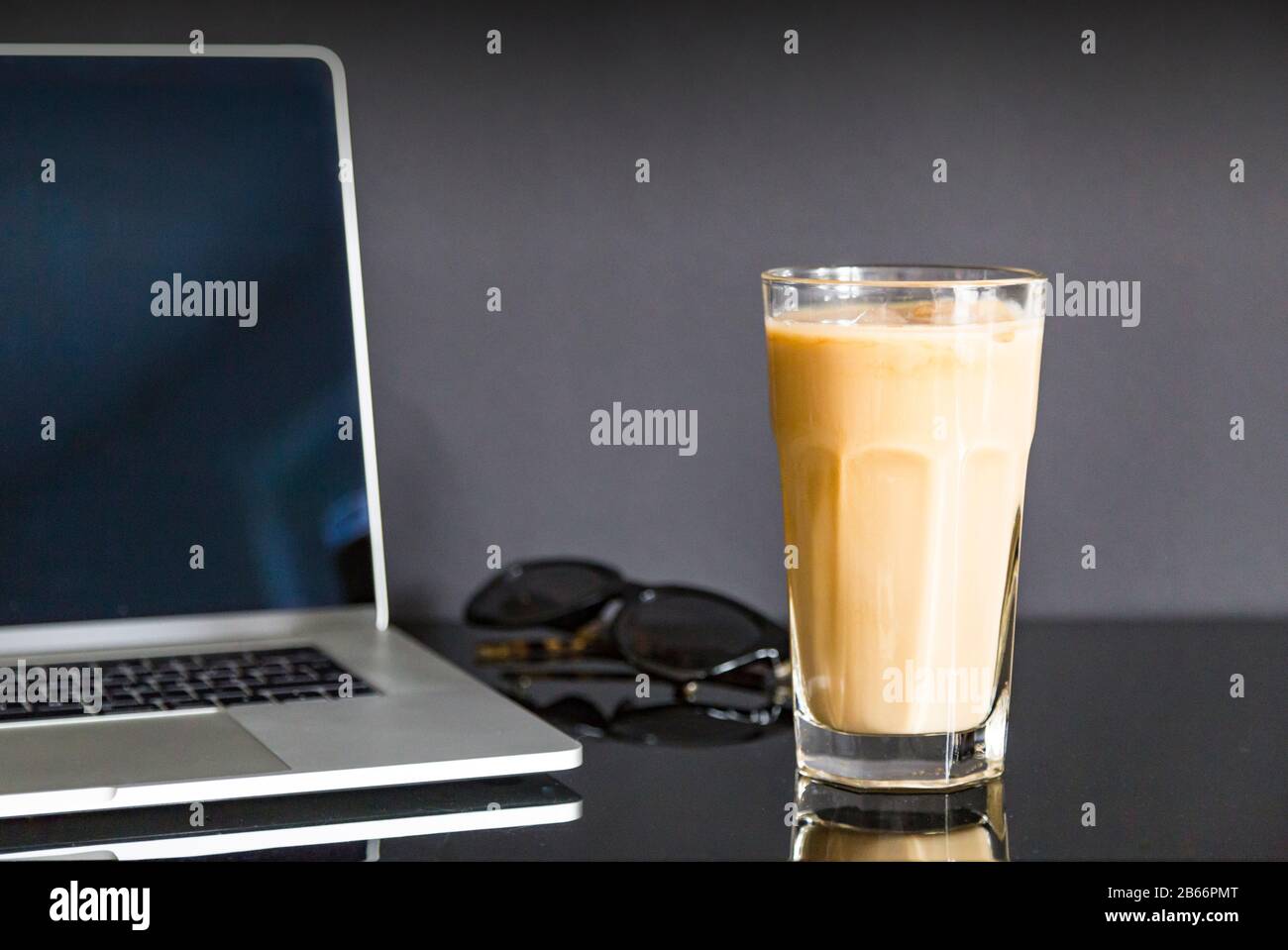 Erfrischender Eiskaffee in moderner Arbeitsumgebung mit Sonnenbrille und Laptop/Notebook. Stillleben, Lifestyle, Business. Stockfoto