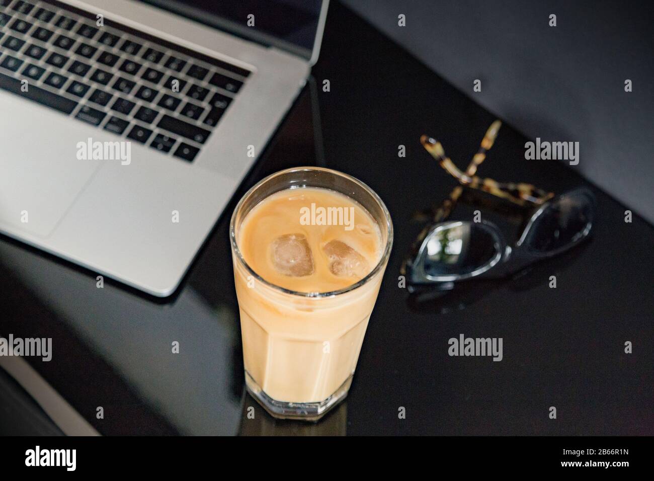 Erfrischender Eiskaffee in moderner Arbeitsumgebung mit Sonnenbrille und Laptop/Notebook. Stillleben, Lifestyle, Business. Stockfoto
