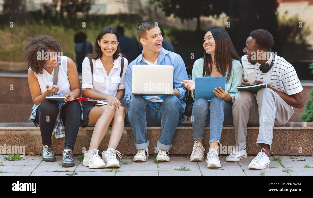 Fröhliche Studenten Der Universität Sitzen Mit Laptop Auf Dem Campus Und Lachen Zusammen Stockfoto