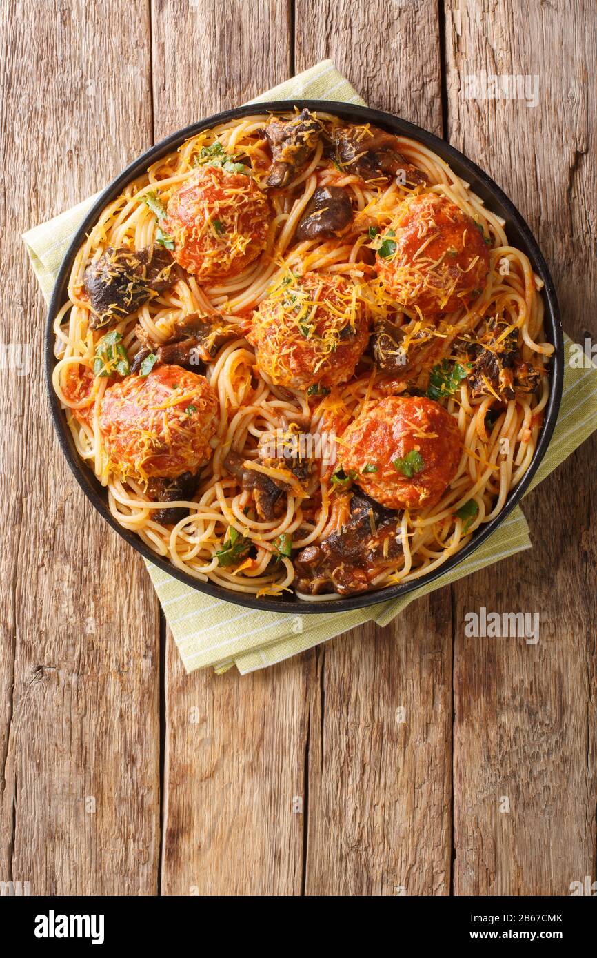 Italienische Fleischbällchen mit einer Beilage aus Spaghetti mit Pilzen und Cheddarkäse in einem Teller auf dem Tisch. Vertikale Draufsicht von oben Stockfoto