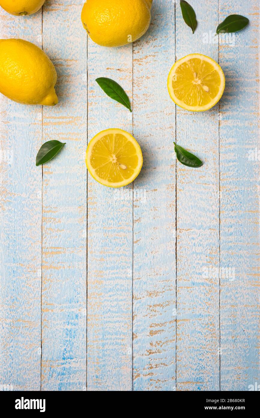 Flache Laienzusammensetzung aus reifen ganzen und halben Zitronen mit Blättern auf hellblauem Holzhintergrund. Kopierbereich, Draufsicht. Stockfoto
