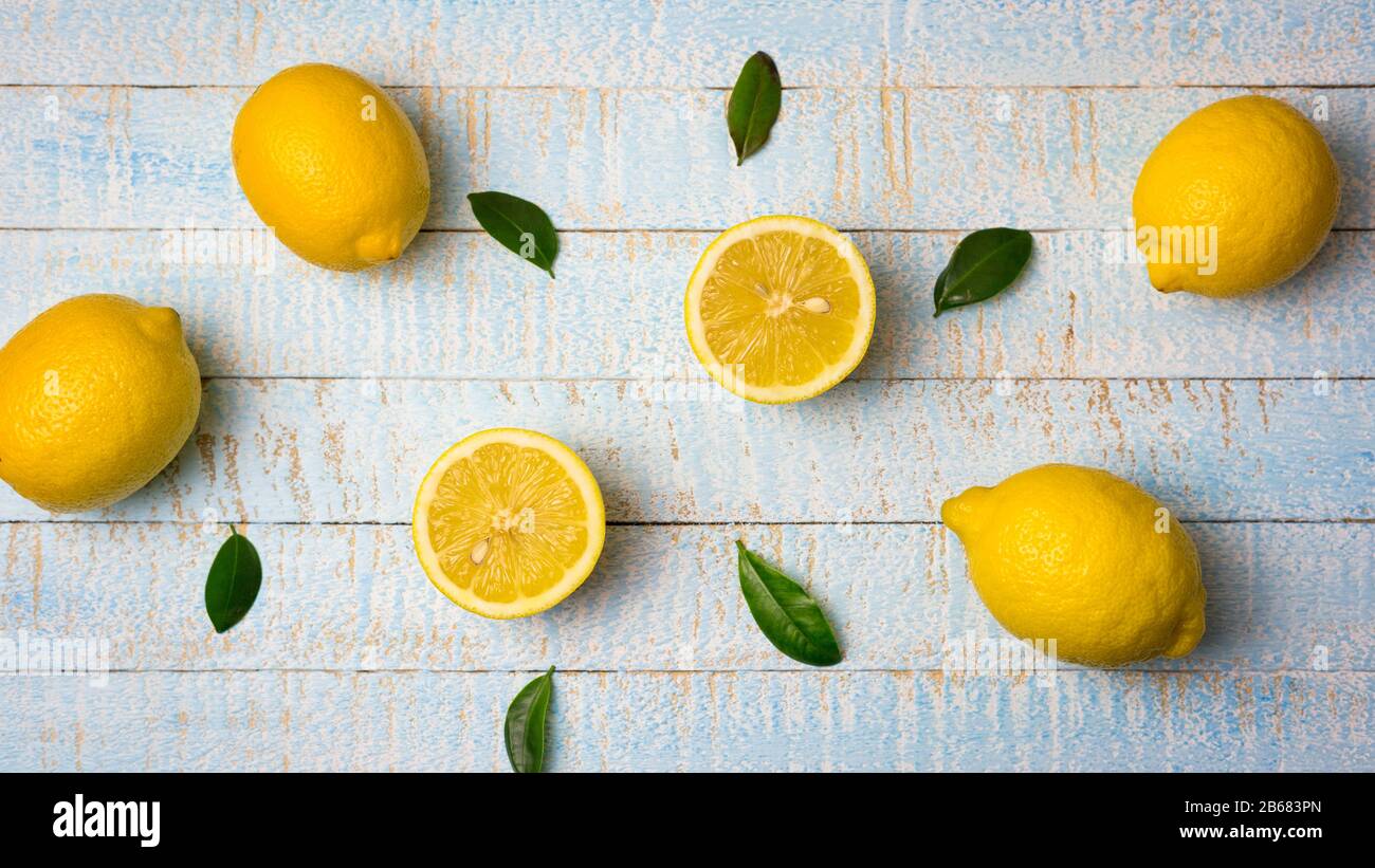 Flache Laienzusammensetzung aus reifen ganzen und halben Zitronen mit Blättern auf hellblauem Holzhintergrund. Kopierbereich, Draufsicht. Stockfoto