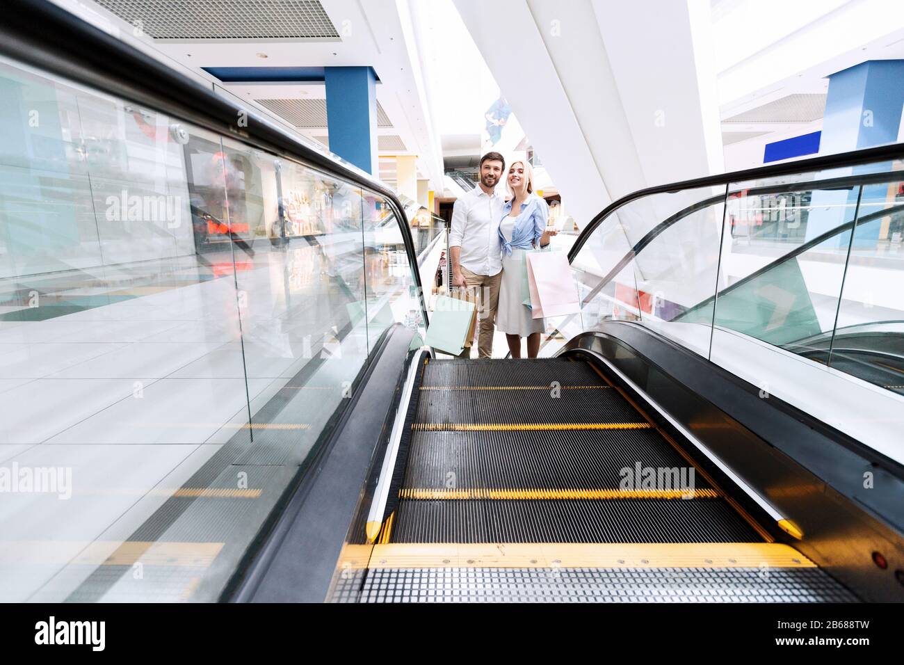 Ehepartner, Die Auf Der Escalator Stairs Holding Shopper Bags In Mall Stehen Stockfoto