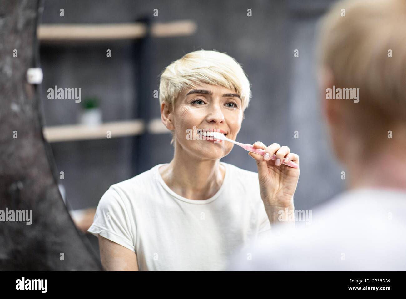 Mittlere Dame, Die Zähne Putzt, Mit Zahnbürste, Die Im Badezimmer Im Innenbereich Steht Stockfoto