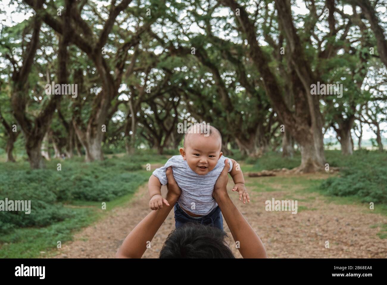 Vater trägt sein Baby auf, während er im Park spazieren geht, während er einen Urlaub genießt Stockfoto