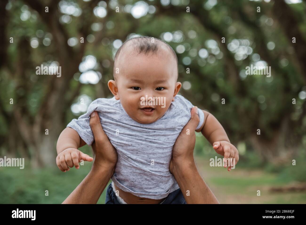 Der kleine Junge lächelt, wenn er nach oben getragen wird, während er einen Urlaub im Park genießt Stockfoto