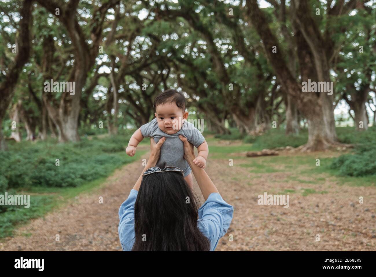 Asiatische Mutter hält ein Baby im Park, während sie gemeinsam Urlaub macht Stockfoto