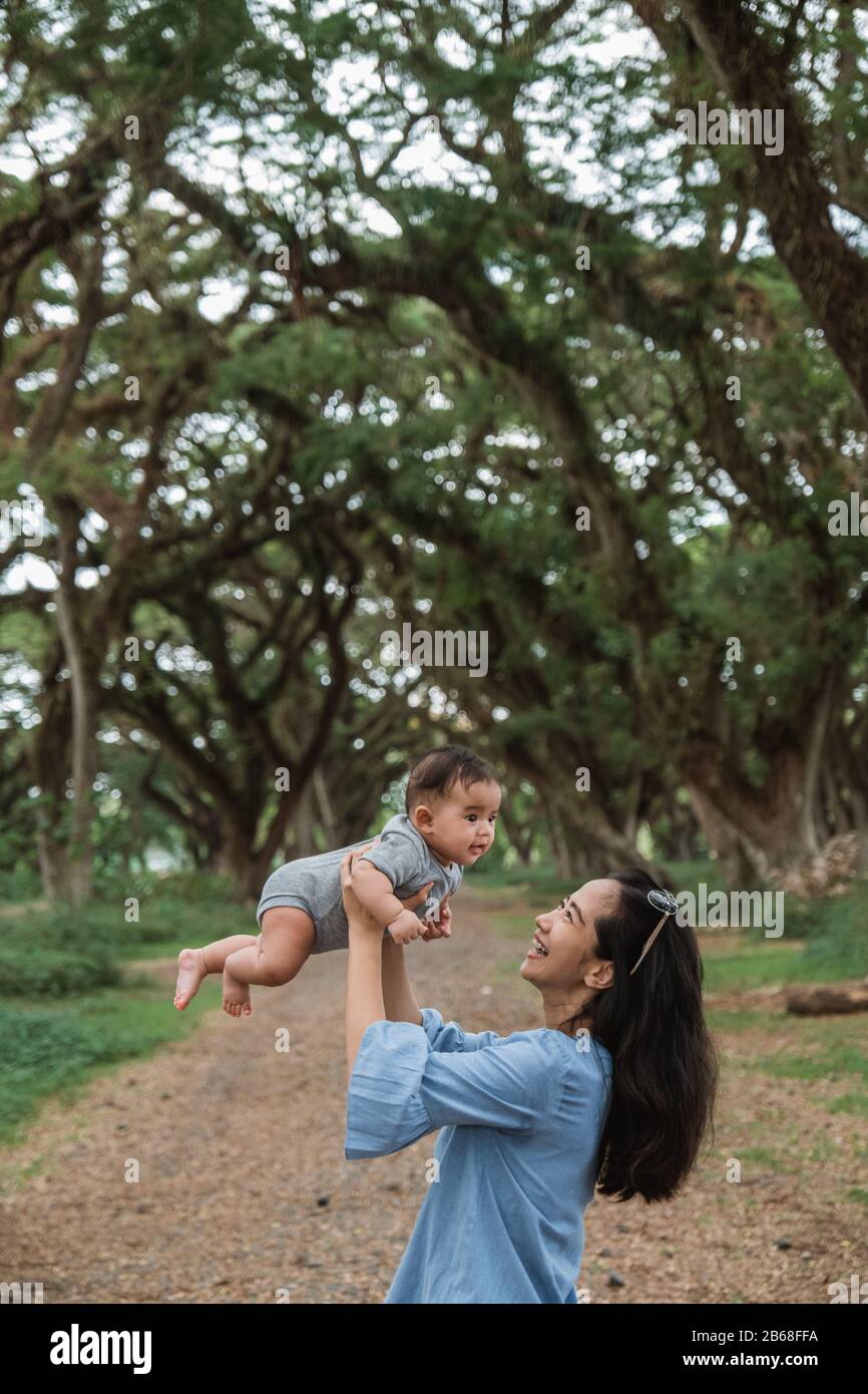 Asiatische Mutter lacht, während sie ein Baby festhält, während sie gemeinsam Urlaub macht Stockfoto