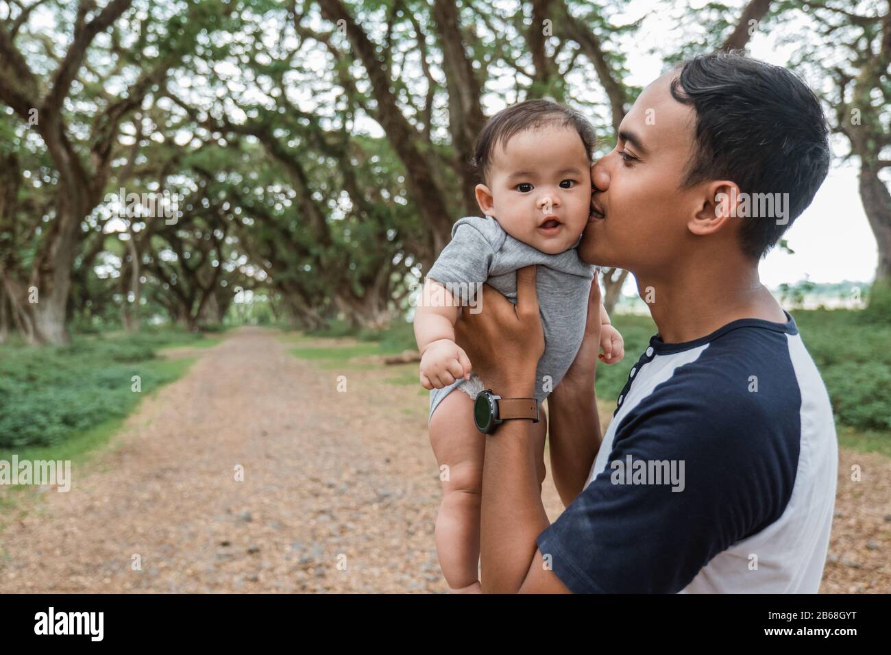 Asiatischer Vater küsst sich, während er ein Baby festhält, während er gemeinsam Urlaub macht Stockfoto