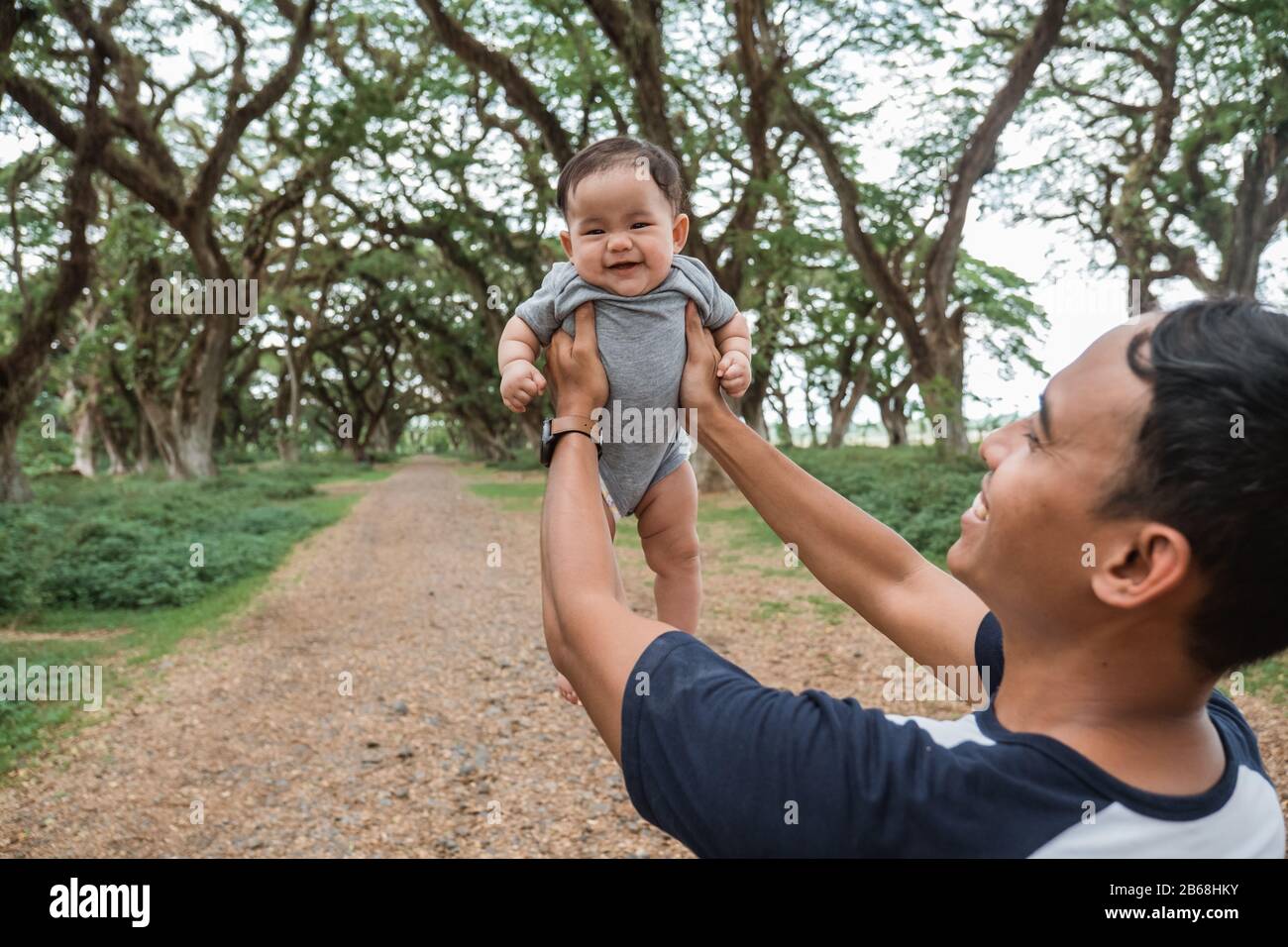 Asiatischer Vater lacht, während er ein Baby festhält, während er gemeinsam Urlaub macht Stockfoto