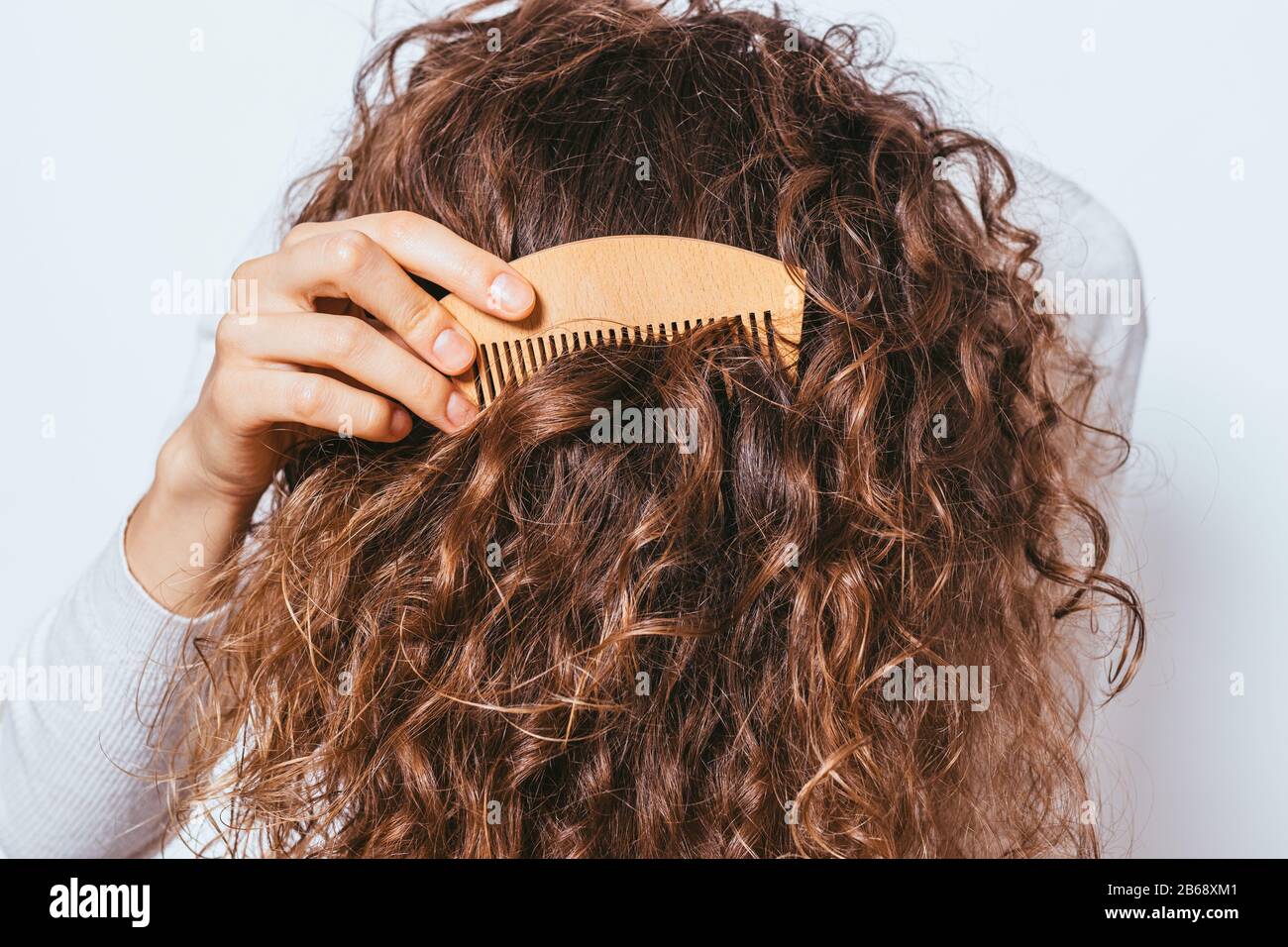Nahaufnahme junge Frau kämmt ihr gesundes dickes lockiges Haar mit Holzkamm. Stockfoto