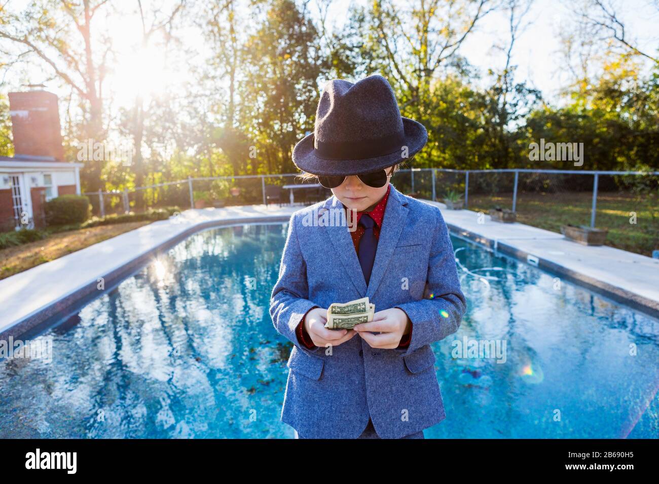 Junge in einem Anzug und dunkle Brille, die am Rande der Wasserzählung von Dollarscheinen steht. Stockfoto