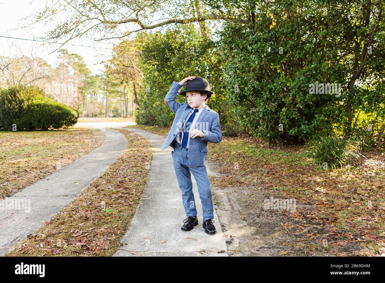 6 Jahre alter Junge, der in Anzug gekleidet und Fedora trägt, in der Einfahrt Stockfoto