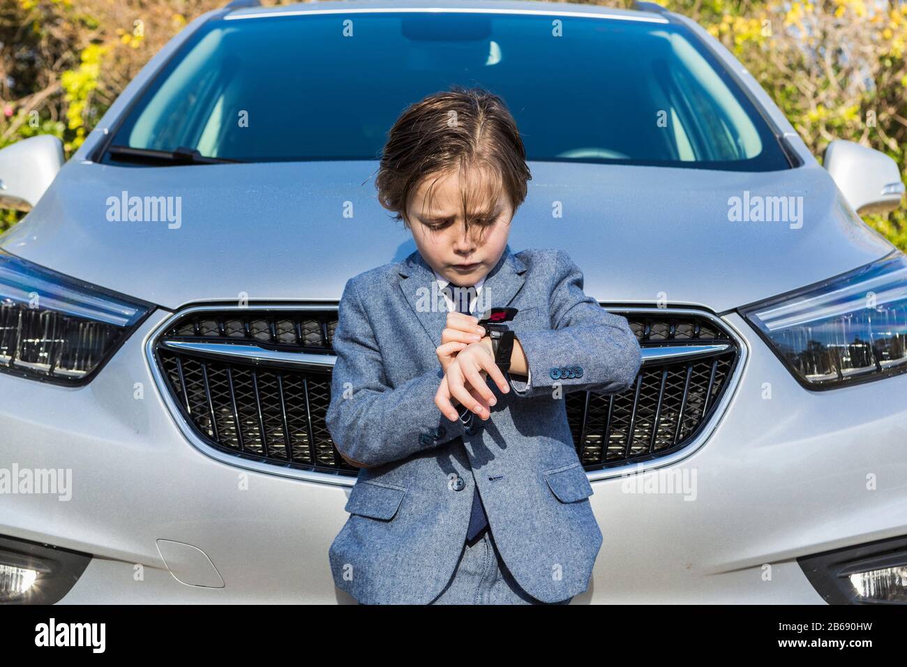 6-jähriger Junge mit Blick auf seine Uhr auf das Auto gelehnt Stockfoto