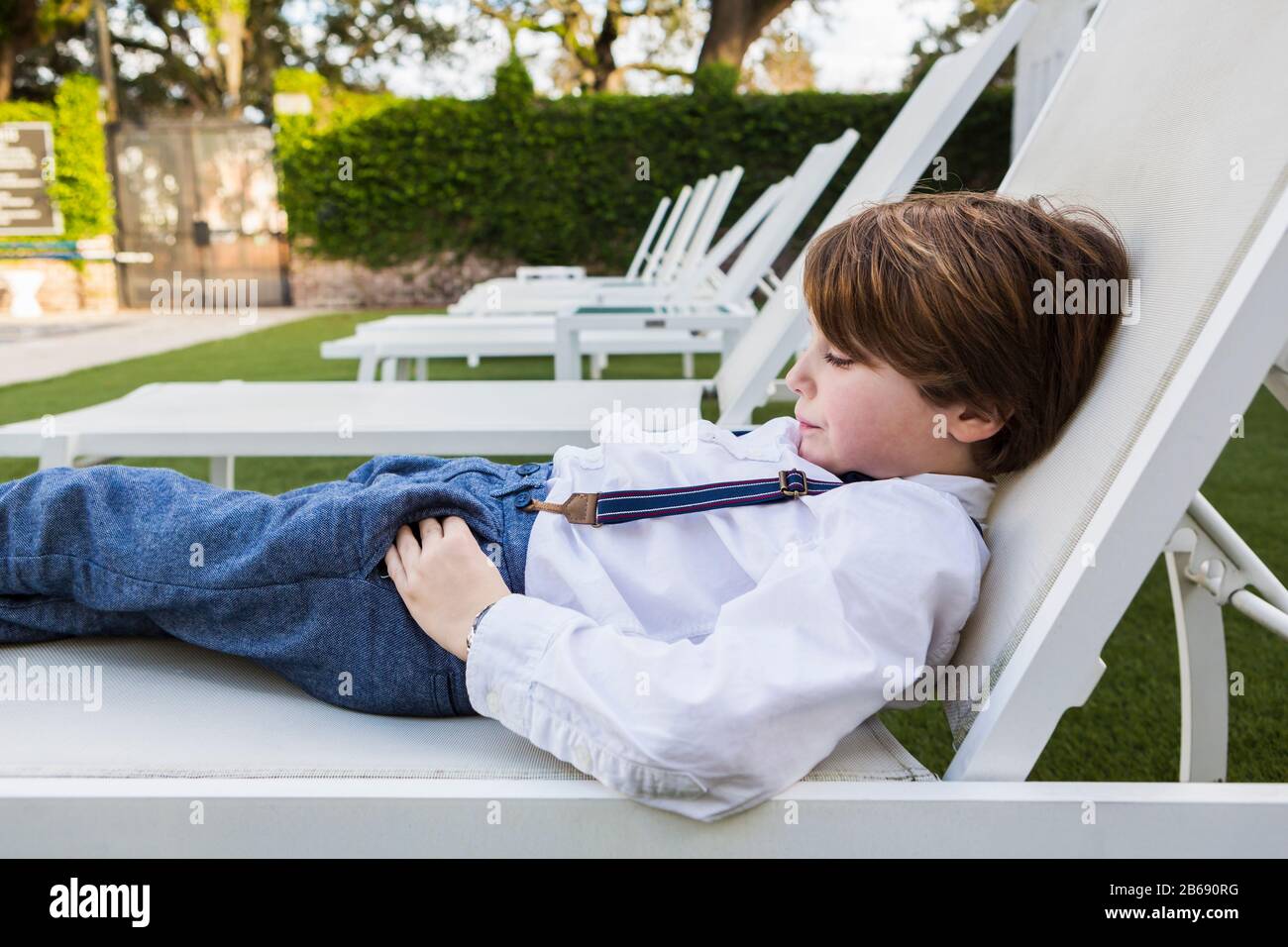 6 Jahre alter Junge, der sich auf dem Liegestuhl zurückschlingende Stockfoto