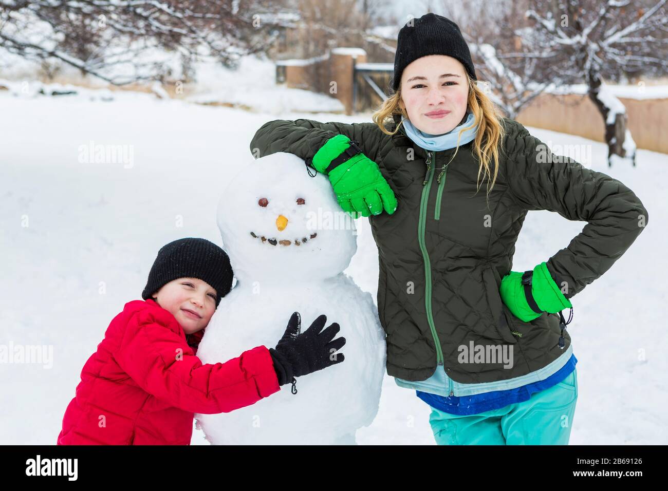 Bruder und Schwester, ein kleiner Junge und Mädchen im Teenager-Alter, die sich im Winter an Schneemann lehnen Stockfoto