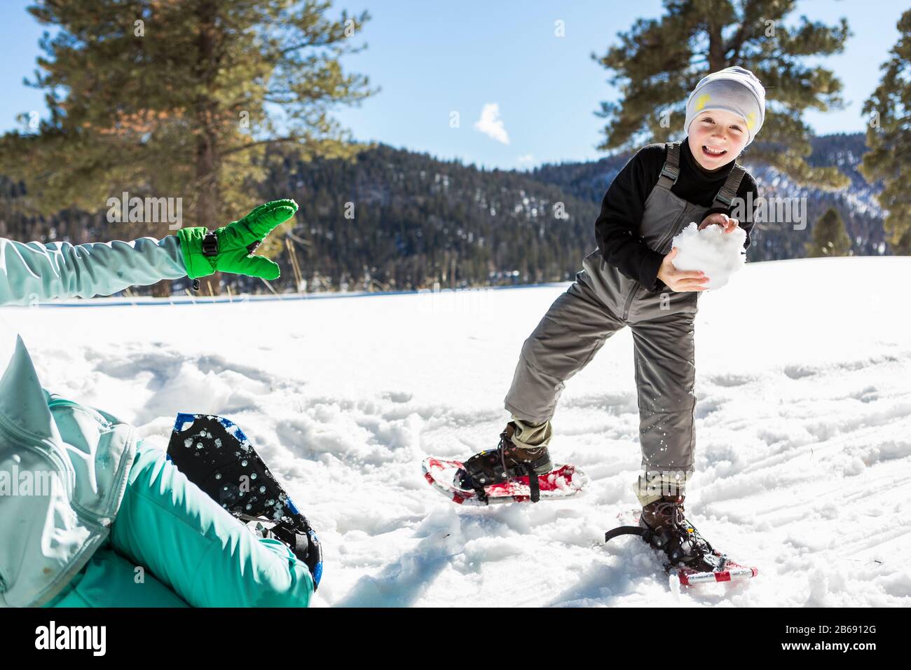 Ein sechs Jahre alter Junge mit Schneeschuhen, der einen großen Schneeball hält. Stockfoto