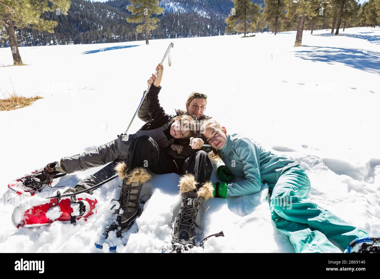 Eine Frau und ihre beiden Kinder, Teenager-Mädchen und ein kleiner Junge, der in Schneeschuhen und Skiausrüstung im Schnee liegt. Stockfoto