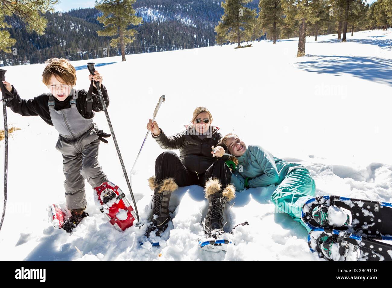 Eine Frau und zwei Kinder in Schneeschuhen im dichten Schnee, Mutter und Tochter lachen auf dem Boden. Stockfoto