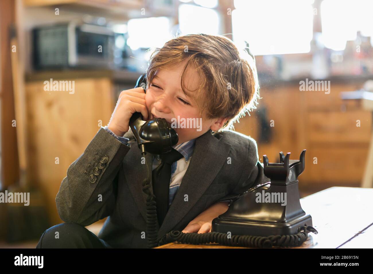 Ein sechsjähriger Junge in einem Anzug und Krawatte, der zu Hause mit einem alten Vintage-Telefon spricht Stockfoto